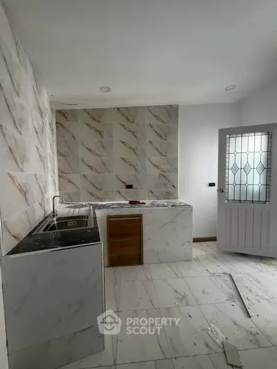 Modern kitchen with marble tiles and sleek design, featuring a stainless steel sink and elegant door.