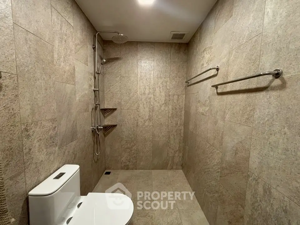 Modern bathroom with sleek shower and toilet in a tiled setting.