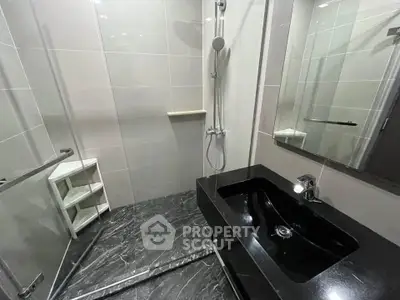 Modern bathroom with sleek black sink and spacious shower area in luxury apartment.