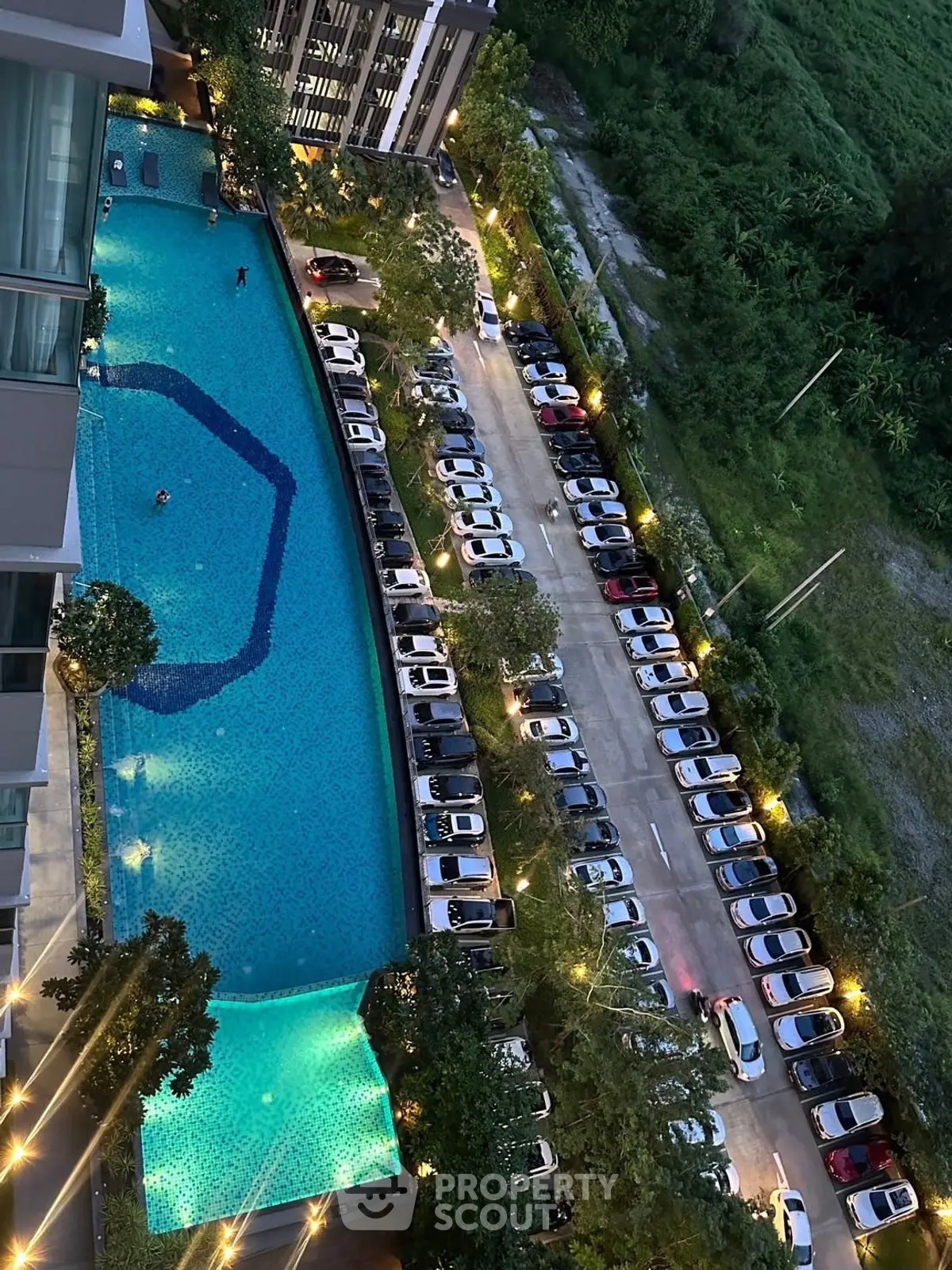 Stunning aerial view of modern apartment complex with illuminated pool and parking area at dusk.
