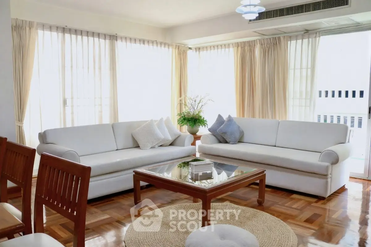 Elegant living room with white sofas and large windows, featuring a cozy atmosphere and natural light.