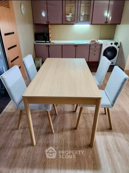 Modern kitchen with wooden dining table and chairs, featuring built-in cabinets and washing machine.