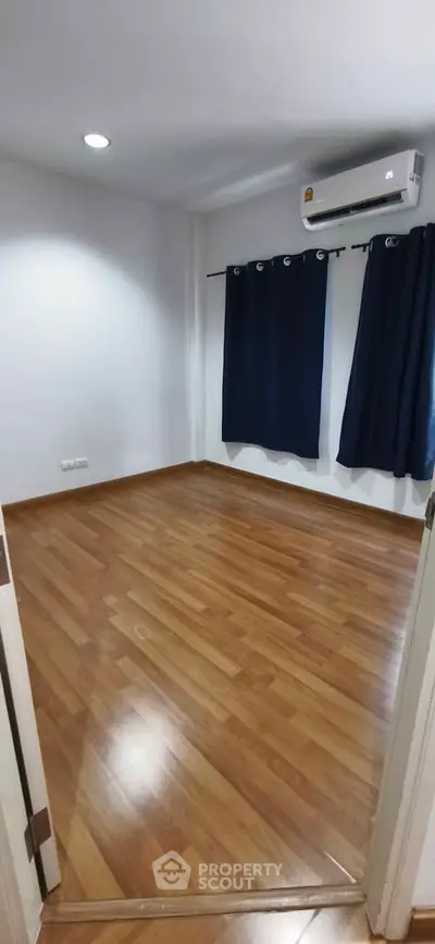 Spacious empty room with wooden flooring and air conditioning, perfect for customization.