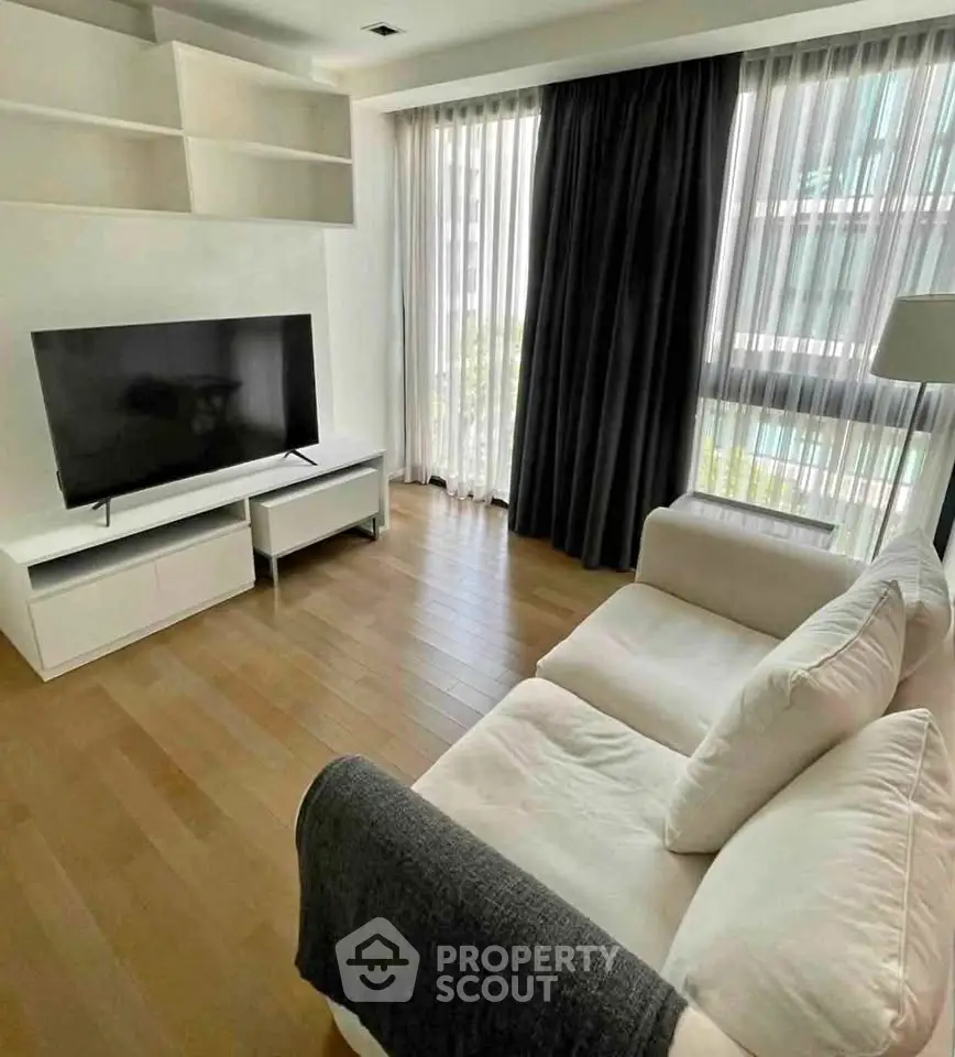 Modern living room with sleek TV setup and cozy sofa, featuring large windows and wooden flooring.