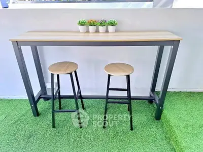 Chic outdoor seating area with modern bar table and stools on green turf.