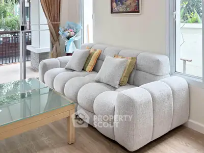Modern living room with plush gray sofa and glass coffee table, overlooking a lush garden view.