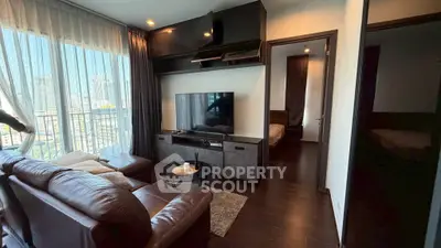 Modern living room with leather sofa and large TV, featuring city view through sheer curtains.