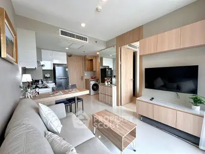 Modern open-layout living room with kitchen, featuring sleek furniture and appliances.