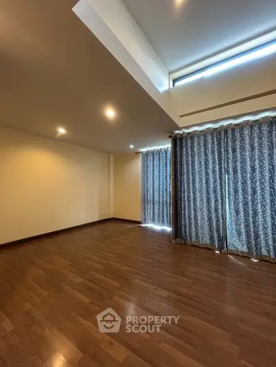 Spacious empty room with wooden flooring and large windows with curtains, ideal for customization.