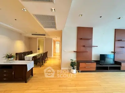 Spacious living room with modern decor and dining area, featuring wooden flooring and stylish shelving.