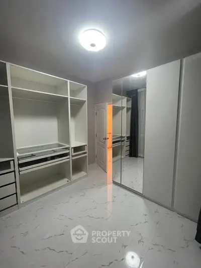 Spacious walk-in closet with modern white cabinetry and mirrored doors