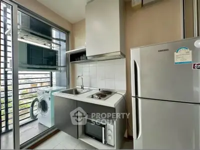 Modern kitchen with balcony view, featuring fridge, microwave, and washing machine for urban living.