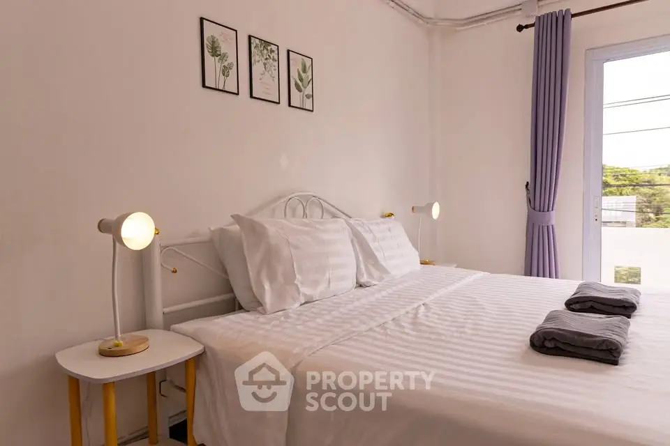 Cozy bedroom with white decor, double bed, and natural light from window.