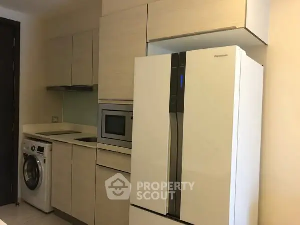 Modern kitchen with sleek appliances including fridge, oven, and washing machine in compact layout.
