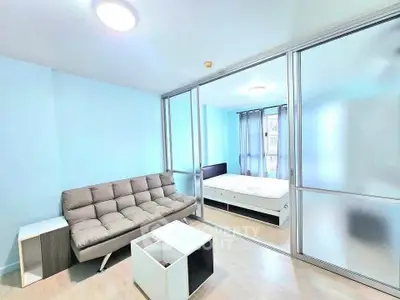 Modern apartment with sliding glass doors separating living room and bedroom, featuring minimalist furniture.