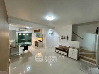 Modern open-plan living area with sleek kitchen and dining space, featuring elegant lighting and staircase.