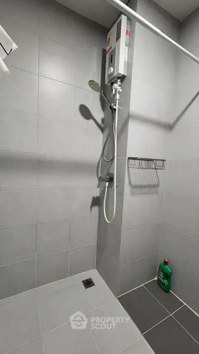 Modern bathroom with sleek gray tiles and shower unit, featuring a wall-mounted water heater.