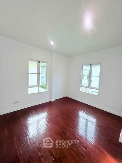 Spacious empty room with polished wooden floors and large windows, perfect for customization.