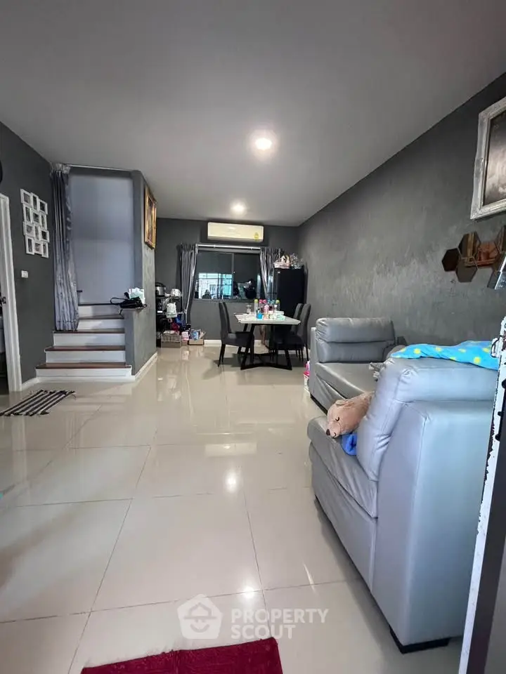Modern living room with sleek gray sofas and dining area, featuring elegant decor and polished flooring.