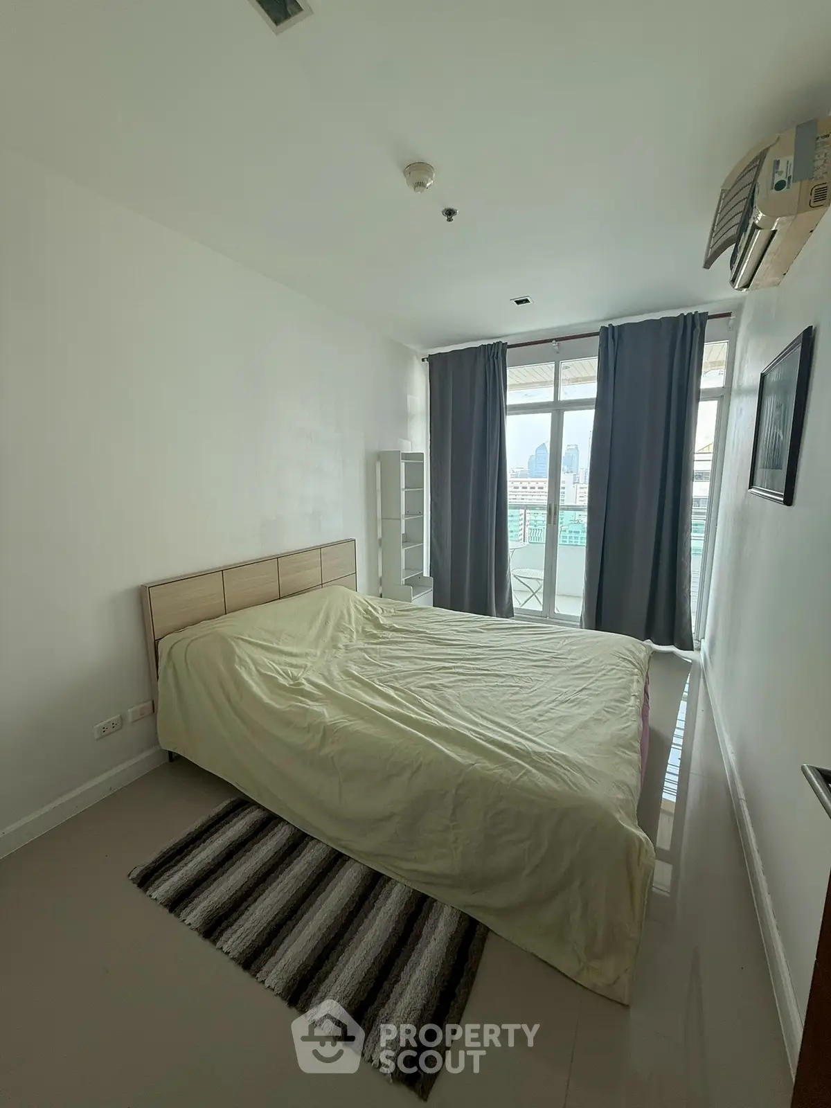 Spacious bedroom with city view and natural light, featuring a cozy bed and modern decor.