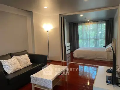 Spacious living room with cozy seating and a view into a serene bedroom with large windows.