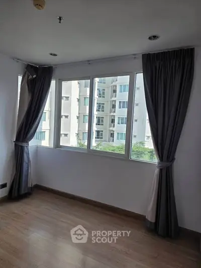 Bright corner unit with large windows and elegant curtains, offering a serene view of neighboring buildings.