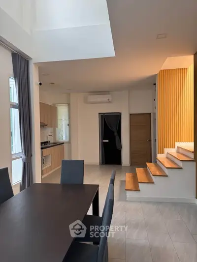 Modern open-plan living area with dining table and stylish kitchen, featuring wooden accents and natural light.