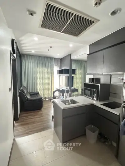 Modern compact kitchen with sleek cabinetry and cozy living area in a stylish apartment.