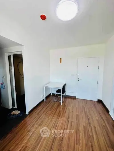 Minimalist room with wooden flooring and white walls, featuring a small desk and chair.