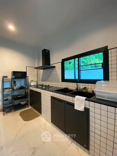 Modern kitchen with sleek black cabinets and tiled backsplash, featuring gas stove and ample natural light.