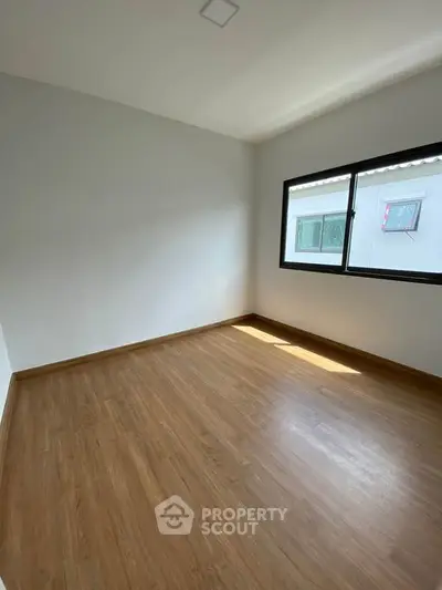 Spacious empty room with wooden flooring and large window, perfect for customization.
