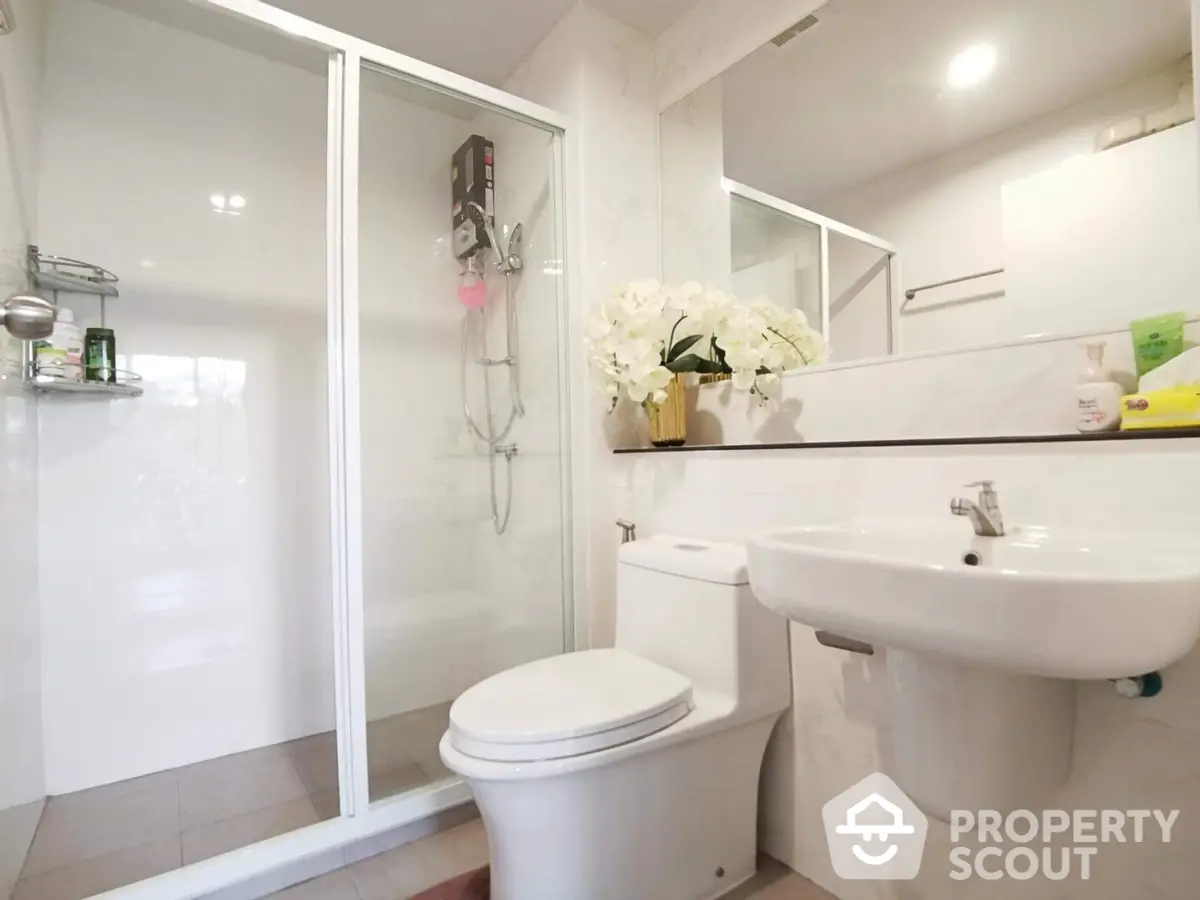 Bright and modern bathroom with a glass-enclosed shower, white fixtures, and elegant floral accents, perfect for a refreshing start to the day.