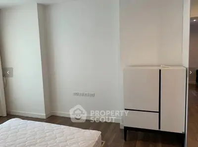 Minimalist bedroom with wooden flooring and modern white furniture, perfect for a cozy living space.