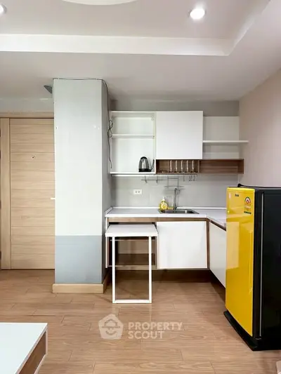 Modern kitchen with sleek cabinets and vibrant yellow fridge in a cozy apartment.