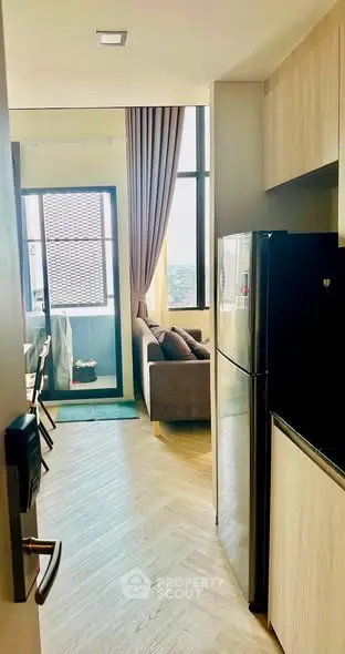 Modern apartment interior with open kitchen and cozy living area, featuring large windows and stylish decor.