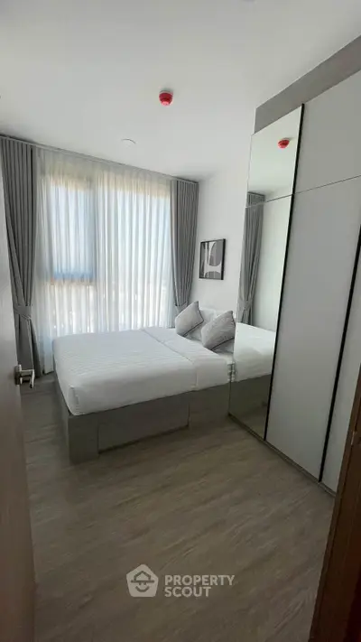 Modern bedroom with sleek design, featuring a large mirror wardrobe and soft natural lighting.