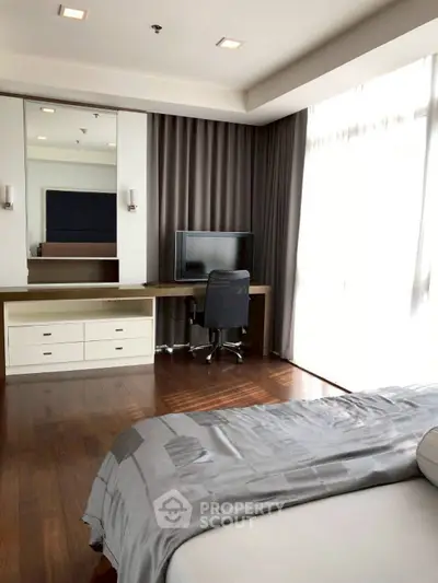 Spacious bedroom with elegant wooden flooring and natural light, featuring a sleek desk and modern decor.