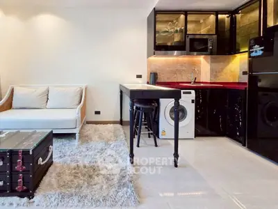 Modern open-plan living room with sleek kitchen and washing machine, featuring stylish black cabinetry and cozy seating area.