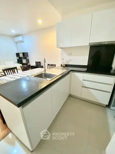Modern kitchen with sleek white cabinets and black countertops in open layout apartment.