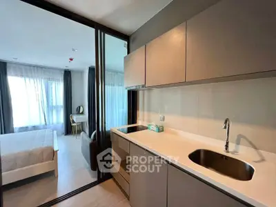 Modern studio apartment with sleek kitchen and cozy bedroom separated by glass partition.