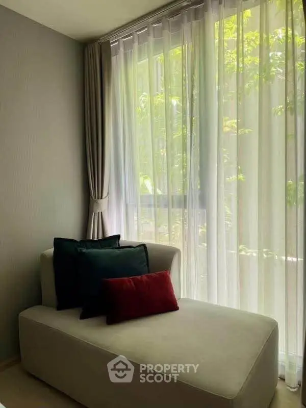 Cozy corner with elegant chaise lounge and lush garden view through sheer curtains.