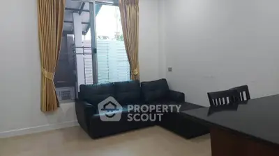 Modern living room with black leather sofa and dining area, featuring large window and golden curtains.
