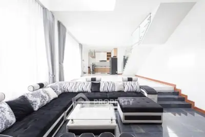 Spacious modern living room with elegant black and white decor and open kitchen layout.