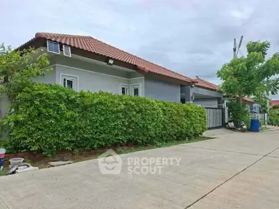 Charming suburban house with red-tiled roof and lush green hedges, perfect for family living.