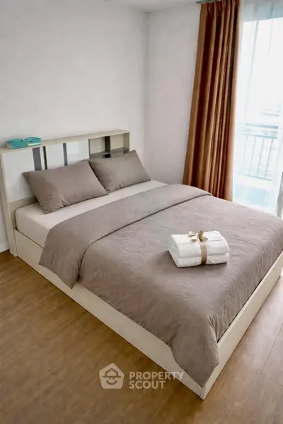 Cozy bedroom with modern decor and natural light, featuring a neatly made bed and wooden flooring.
