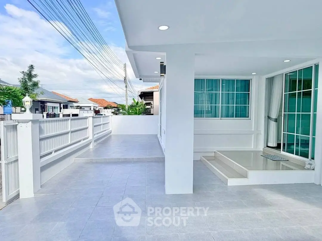 Modern white house exterior with spacious tiled patio and large windows.