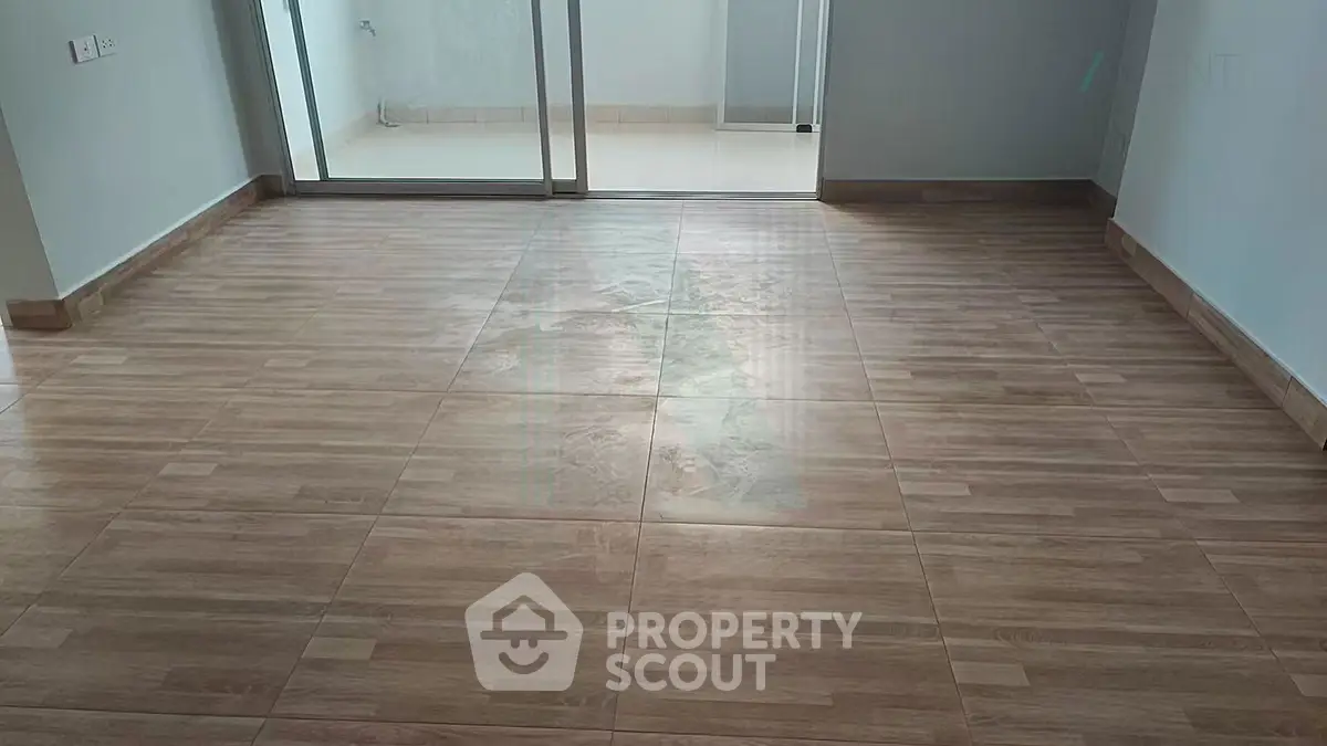 Spacious empty room with wooden tile flooring and sliding glass doors leading to a balcony.
