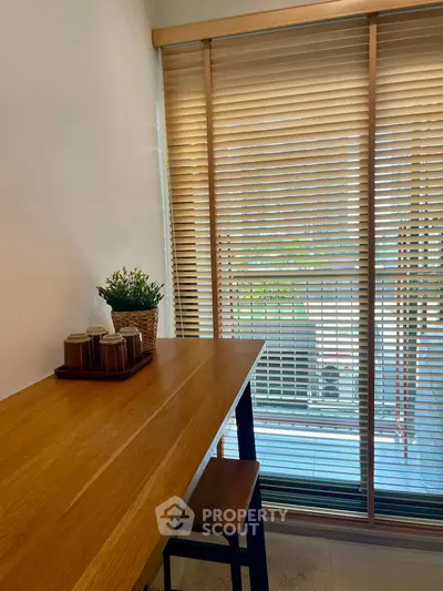Cozy study nook with wooden desk and window blinds, perfect for focused work.
