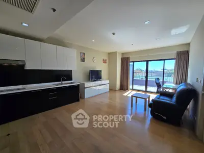 Spacious modern living room with open kitchen and large windows offering natural light and city view.