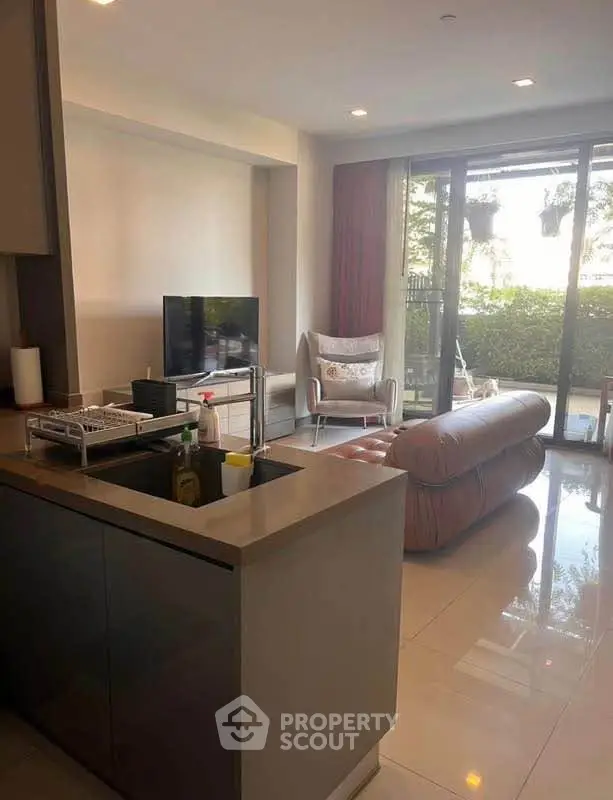 Modern living room with open kitchen and garden view, featuring sleek furniture and natural light.